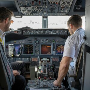 Two pilots navigating an aircraft cockpit, focused on advanced avionics and flight systems.